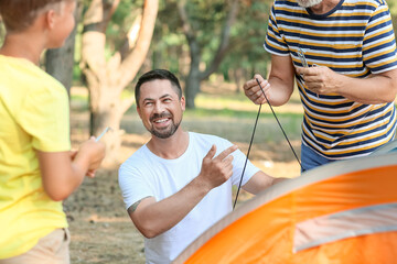 Handsome man putting up camping tent with his father and little son in forest - Powered by Adobe