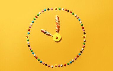 Clock made of colorful candies and lollipops on color background