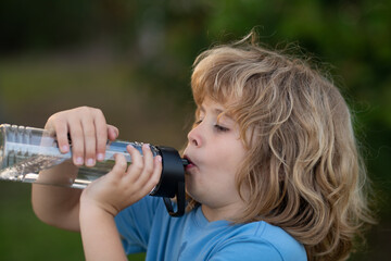 Kid drinking water outdoor. Close up portrait of boy drink water from bottle in the garden.