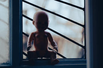 baby doll sits near the window. child accident concept