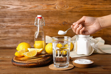 Woman pouring baking soda into glass with water on wooden background