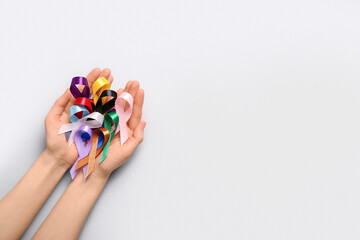 Female hands full of awareness ribbons on light background. World Cancer Day