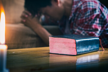 Bible of christian on wooden table with a man praying at behind.
