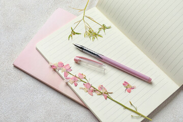 Notebooks, pen and dry flowers on light background