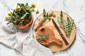 Yellow dandelions with wooden boards, bowl and knife on light background