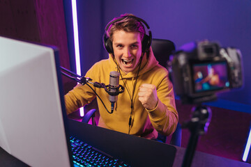 Exited caucasian cyber sportsman shooting vlog, screaming happily on camera, because he won the game, celebrating his victory, make yes hand gesture. Pro gamer influencer has live video stream. Esport