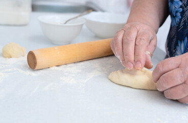 Senior woman hands making pies with apple filling on a white kitchen table with wooden rolling pin on background. Selective focus. Cooking at home concept. Tradition home-made food