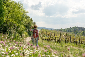Woman with brown hair, gray t-shirt, jeans and red backpack, touching her straw hat while hiking in...