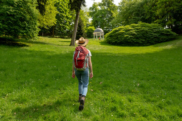 Woman with brown hair, gray t-shirt, jeans, straw hat and red backpack hiking on a meadow at Freundschaftstempel temple, Staatspark Fürstenlager, Auerbach, Bensheim, Germany