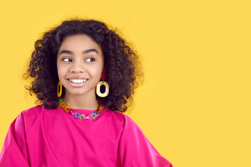 Beautiful Black kid in cool outfit with bijouterie isolated on yellow background. African girl with happy face expression looks sideways at blank marketing text copy space. Children's fashion concept