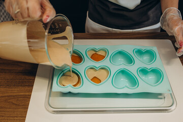 Woman confectioner pouring liquid chocolate into rubber mold tray for cooking pastry candy. Female...