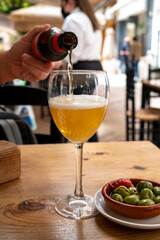 Pouring of beer from bottle in Spanish outdoor cafe, tapas bowl with green olives