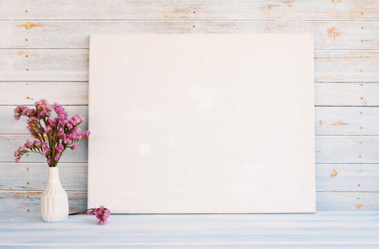 White canvas hanging on light blue wooden wall. Mockup, wall decor, blank canvas stretched on stretcher bar