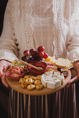 A woman in lace blouse holds in her hands a round wooden cutting board with Wine appetizers -...