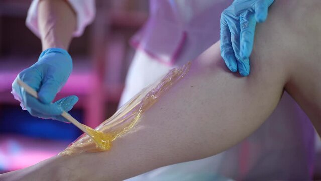 hands in blue disposable gloves are applied with a special shovel to the shugaring mass on the shin, then torn off