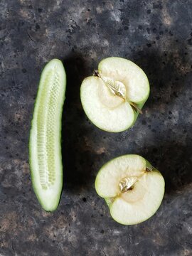 Halves of green apple and slice of fresh cucumber on black concrete background with copy space.