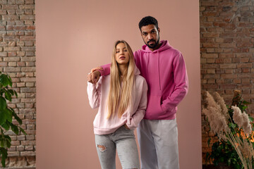 Fashion studio portrait of a happy young couple in hoodie posing over pink background.