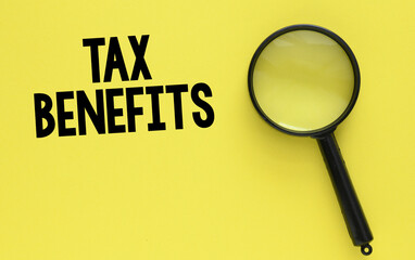 TAX BENEFITS words on yellow paper next to a black magnifier. Finance and business concept.