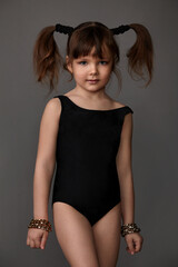 pretty little girl in a black sports swimsuit and ponytails on her head posing in the studio on a...