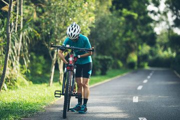 Obraz na płótnie Canvas Woman cyclist adjust the seat height cycling on summer park trail