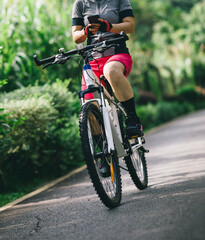 Fototapeta na wymiar Woman using smart phone cycling on tropical park trail in summer