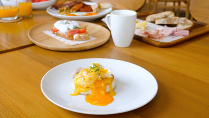 Cut egg benedict with liquid yolk on english muffin in restaurant. Classic poached egg with hollandaise sauce sandwich on white plate on table in cafe. Breakfast, lunch or brunch set food concept.