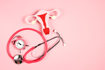 Women's health awareness concept. Uterus symbol with stethoscope and alarm clock on pink background.