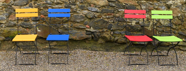 Vier leere Gartenstühle vor einer steinernen Mauer
