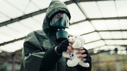 Man wearing a gas mask finds a stuffed animal in a war-torn hospital