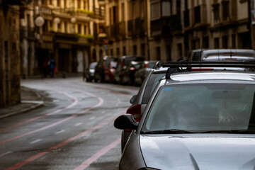 Row of cars parked along the street and old buildings in Europe city. Many cars parked on road in old town. City street in Europe. Front view of car parked outside residential building. City traffic.