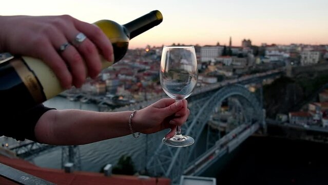 Authentic shot of unrecognizable hand pouring red wine to the glass. Oporto, Douro valley on the background. Enjoying red wine at Portugal, Porto, Port wine. Sunset colors on the background.
