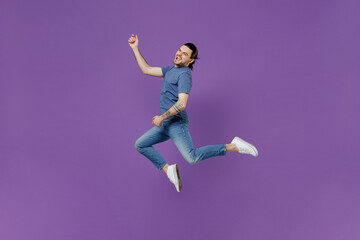 Fototapeta na wymiar Full body young expressive singer rocker cool man 20s wearing basic blue t-shirt jump high do playing guitar gesture isolated on plain purple color background studio portrait People lifestyle concept