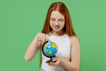 Little redhead kid smiling happy cool girl 12-13 years old wearing white tank shirt hold in hands spin Earth world globe isolated on plain green background studio portrait Childhood lifestyle concept