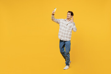 Fototapeta na wymiar Full body young smiling happy cheerful caucasian man 20s wearing white casual shirt doing selfie shot on mobile cell phone post photo on social network show v-sign isolated on plain yellow background