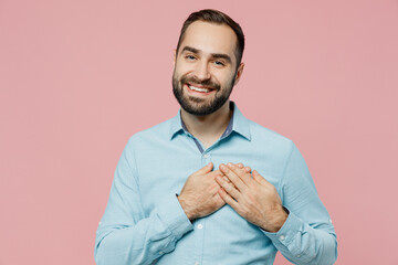 Young smiling kind-hearted happy fun caucasian man 20s wearing classic blue shirt put folded hands on heart isolated on plain pastel light pink background studio portrait. People lifestyle concept