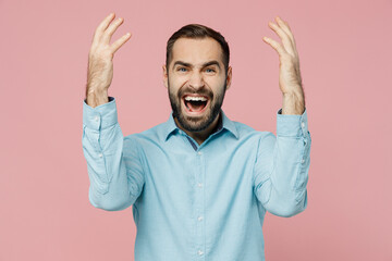 Young angry mad furious dissatisfied man 20s wearing classic blue shirt look camera spread hands scream shout isolated on plain pastel light pink background studio portrait. People lifestyle concept.