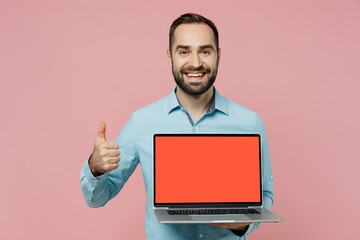 Young fun caucasian man 20s wear classic blue shirt hold use work on laptop pc computer with blank screen workspace area show thumb up gesture isolated on plain pastel light pink background studio