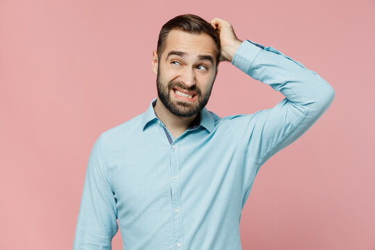 Young puzzled caucasian man 20s wear classic blue shirt look aside on workspace area mock up scratch hold head isolated on plain pastel light pink background studio portrait. People lifestyle concept.