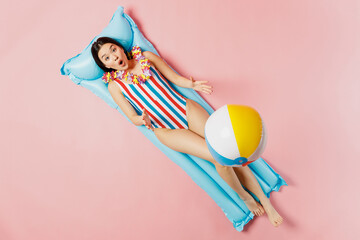 Top view full size woman of Asian ethnicity in striped swimsuit hawaii lei lie on inflatable...
