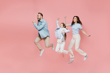 Fototapeta na wymiar Full size young happy fun parents mom dad with child kid daughter teen girl in blue clothes jump high do winner gesture clench fist isolated on plain pastel light pink background. Family day concept.