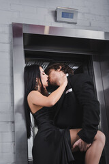 Passionate young couple in formal wear kissing near elevator.
