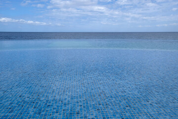 Fototapeta na wymiar Blue clear water surface in swimming pool outdoor with sea view, horizon. Water texture for background. Summer and vacation concept. Ripples on water. Blue tile fine mosaic in swimming pool.