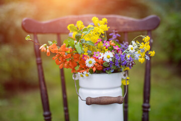 bukiet wiosennych, polnych kwiatów w rustykalnym klimaci w kance na mleko na starym krześle w ogrodzie w promieniach słońca, wiejskie klimaty - obrazy, fototapety, plakaty