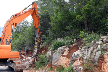 Excavator crusher machine breaks rocks to widen road