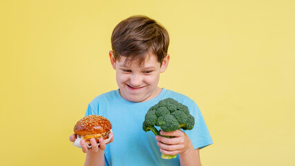The boy is holding a broccoli and a burger.
Portrait of a funny boy in a blue T-shirt, on a yellow...