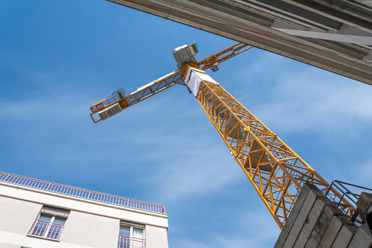Building under construction and orange crane among city walls