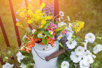 bukiet wiosennych, polnych kwiatów w rustykalnym klimaci w kance na mleko na starym krześle w ogrodzie w promieniach słońca, wiejskie klimaty - obrazy, fototapety, plakaty
