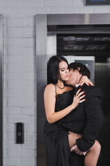 Brunette man in suit kissing sexy woman in dress near elevator.