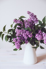 Beautiful fresh lilac flowers in full bloom in vase against white background. Minimalist floral still life.