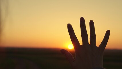 Hand of happy girl at sunrise. Sunset, sun between fingers of girl's hand. Young free woman stretches out her hand to sun, dreams in nature. Child's play hand to sun. Happy family. Beach sunset on sea